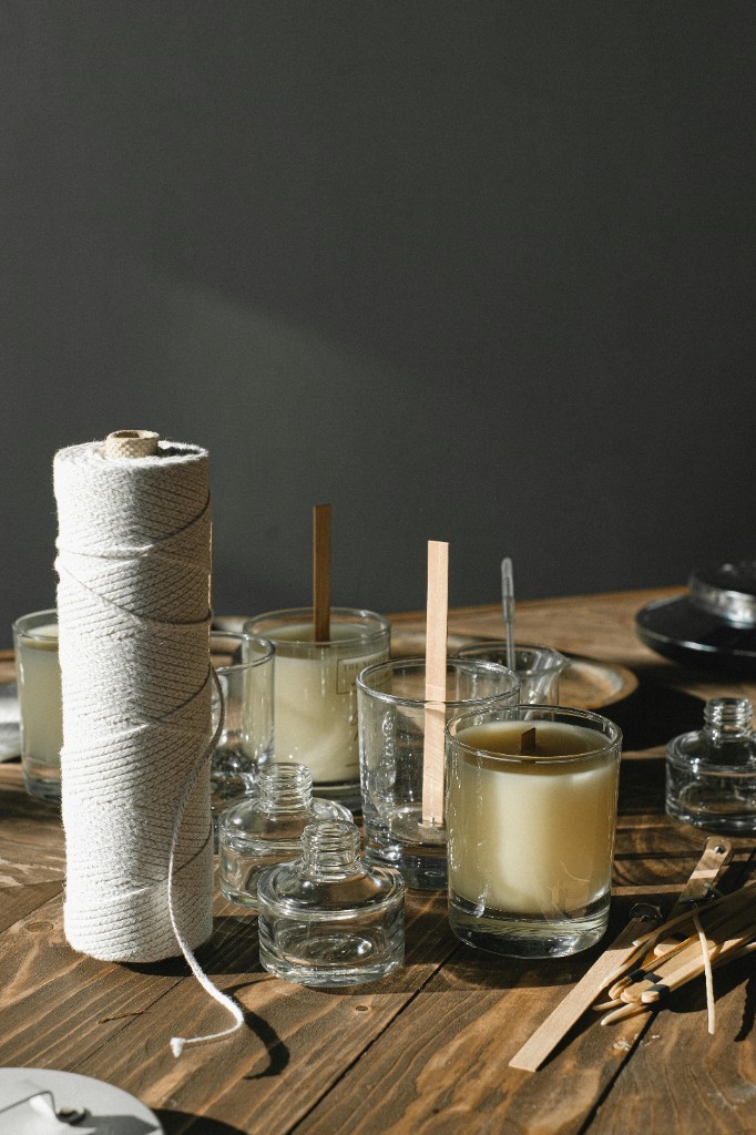 Candle jars, melted wax, and wicking tools arranged on the craft bench